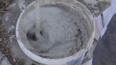 Erkek alçıları. İnşaatçı, inşaat alanındaki sepetin içinde su olan bir bina mikseri kullanarak duvarları sıvamak için karışımı yoğuruyor. İnşaat çalışmaları.
