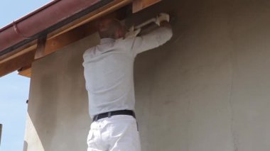 Erkek sıva ustası binanın ön cephesini sıva ile kaplıyor iskele üzerinde duruyor, binanın ön cephesini onarıyor. İnşaat alanında. İnşaat çalışmaları..