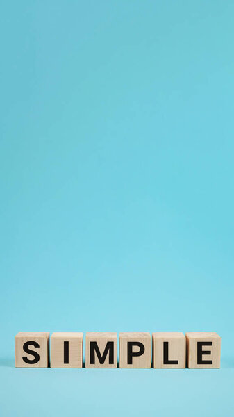 SIMPLE word from wooden blocks with letters, to make something easy, keep it simple concept, blue background.