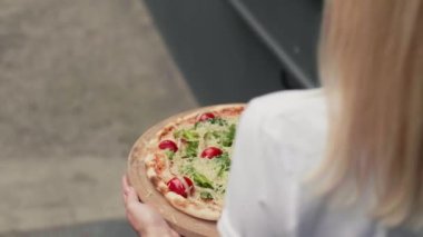 a girl with blond hair and a white shirt carries a pizza to serve on the table