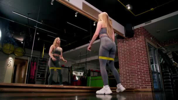 スポーツ女性は黄色のゴムバンドでうずくまっています トラックスーツの女性体操 筋肉を訓練するための動機 スポーツボディコンセプト — ストック動画