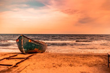 Güneş batarken kumlu sahilde eski paslı ve ahşap bir tekne.