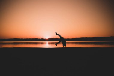 Gün batımında sahilde yoga yapan bir kadının silüeti.