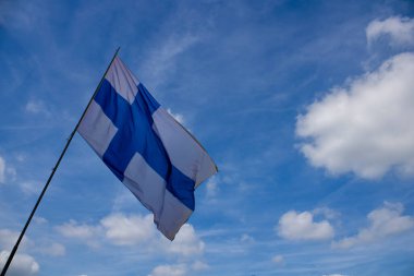 Finlandiya bayrağı, arkasında beyaz bulutlar bulunan mavi bir gökyüzü.