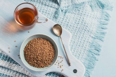 Bir kase çemen otu tohumu ve Mısır çemen otu sarı çayı ya da Methi Dana açık mavi arka planda içer.