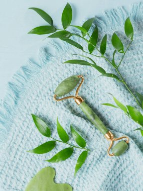 Masaj masörü, iki kafalı ve açık mavi arka planda yeşil taştan bir kazıyıcı. Güzellik yüz masajı terapisi, SPA kişisel bakım konsepti.