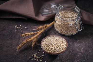 Koyu arka planda bir kase çiğ inci arpa gevreği. İnci arpa lapası pişirme kavramı.