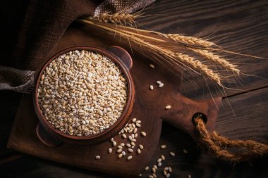 Koyu ahşap arka planda bir kase çiğ inci arpa gevreği. İnci arpa lapası pişirme kavramı.