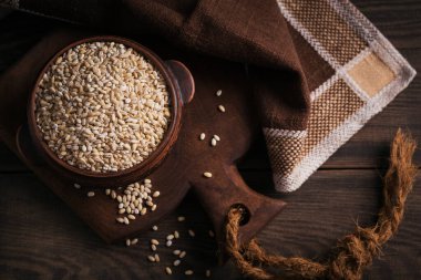 Koyu ahşap arka planda bir kase çiğ inci arpa gevreği. İnci arpa lapası pişirme kavramı.