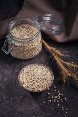 Koyu arka planda bir kase çiğ inci arpa gevreği. İnci arpa lapası pişirme kavramı.