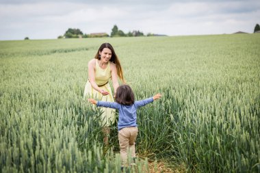 Anne ve küçük doğulu yakışıklı erkek bebek tarlada yürüyor.