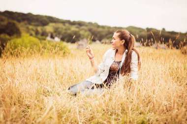 Kırsalda bir tarlada oturan kendine güvenen otantik genç bir kadının portresi.
