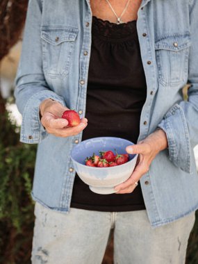 Bir kase olgun çilek tutan yaşlı bir kadının elleri.