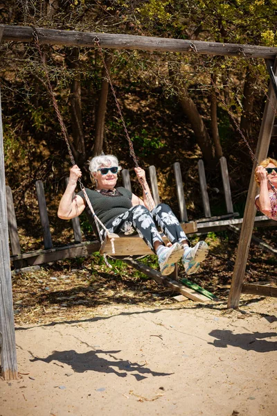 Two elderly women joyfully swinging on a swing and having fan. Happy retirement concept