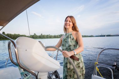 Geminin dümenini tutan uzun elbiseli cesur bayan kaptan. Yat süren kız.