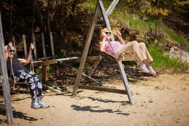 Salıncakta sallanan ve yelpaze tutan iki yaşlı kadın. Mutlu emeklilik kavramı