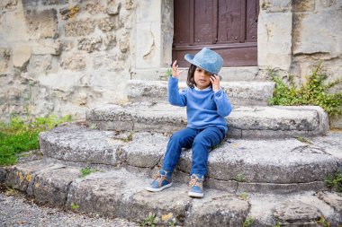 Little handsome baby boy sitting on ancient stone stairs and playing outdoor with straw hat in old city