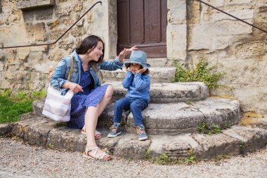 Anne ve küçük yakışıklı erkek bebek antik taş merdivenlerde oturup hasır şapkayla dışarıda oynuyorlar.