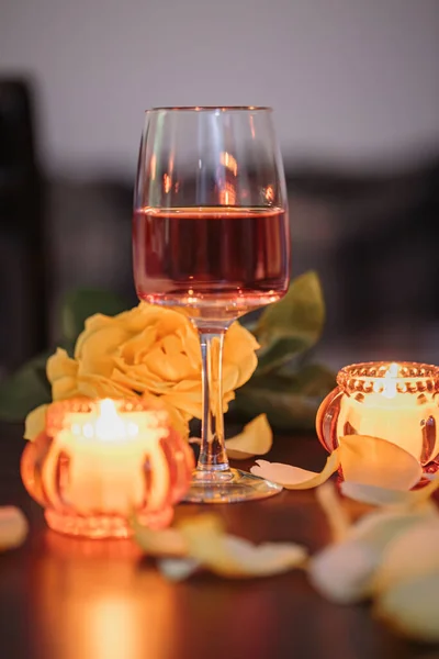 A glass of rose wine, two candles and rose petals on a dark table. Nice evening romantic atmosphere