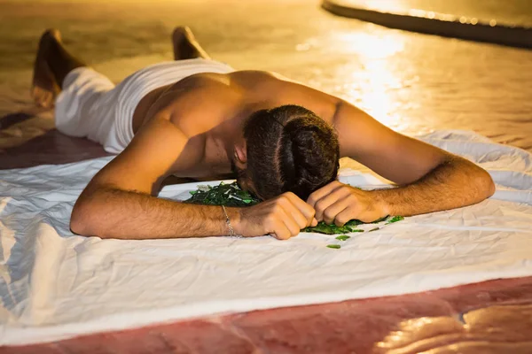 Actor fakir stuntman lies face on broken glass. Night performance yogi show on stage of the hotel in Egypt