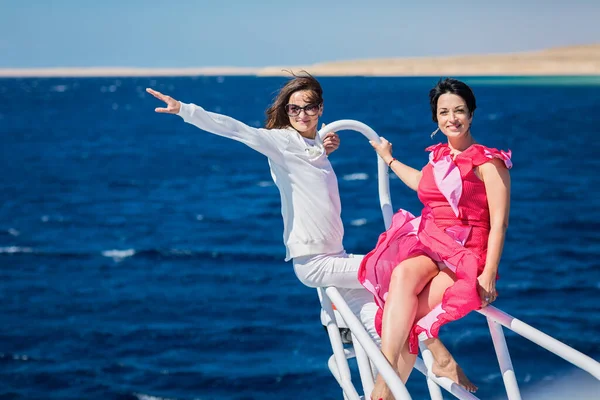 Two women relaxing together on the nose of the yacht at a sunny summer day at sea and enjoying at vacation and luxury travel on boat