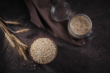 Kurutulmamış organik arpa gevreği, beyaz ahşap arka planda buğday kulakları olan bir kasede. Sağlıklı ve diyet gıda konsepti.