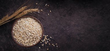 Koyu arka planda bir kase çiğ inci arpa gevreği. İnci arpa lapası pişirme kavramı.