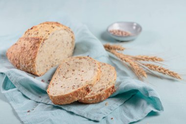 Dilimlenmiş taze kepekli kepek ekmeği keten tohumu ve açık mavi tahtada susam tohumları. Fırın ürünleri