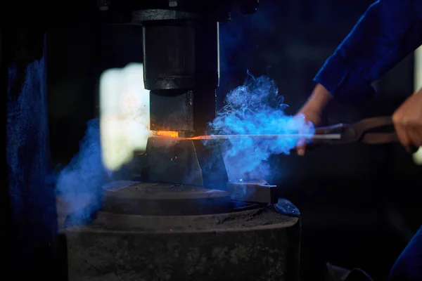 Řemeslník vkládající vyhřívaný kov pod lisovací stroj — Stock fotografie