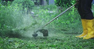 Çalışan adam elektrikli çim biçme makinesiyle çim biçiyor.