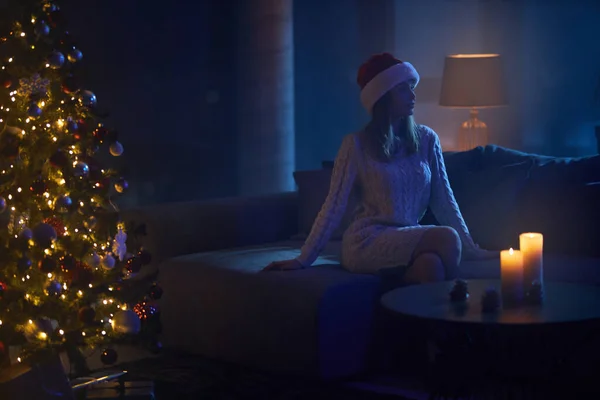 Жінка в капелюсі Санта сидить на дивані біля ялинки — стокове фото