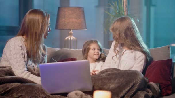 Две девочки и их мать сидят на диване с ноутбуком — стоковое видео