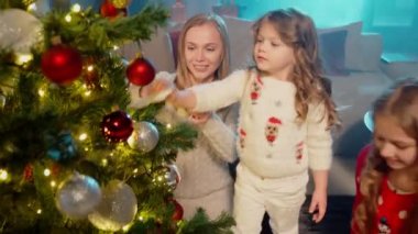 İki kız annelerinin Noel ağacını süslemesine yardım ediyor.