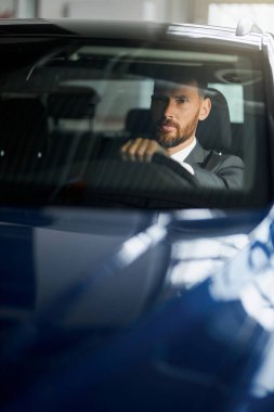 Şık takım elbiseli başarılı bir adam galeride arabaları inceliyor.