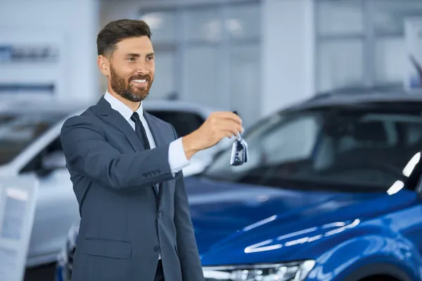 Счастливый человек позирует в современном автомобильном центре с ключами в руках — стоковое фото