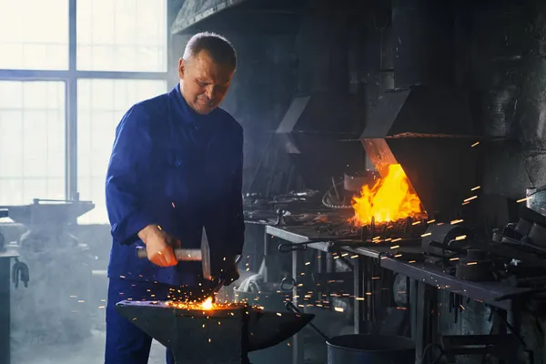 Zralý muž zpracování horký kov s kladivem v kovárně — Stock fotografie