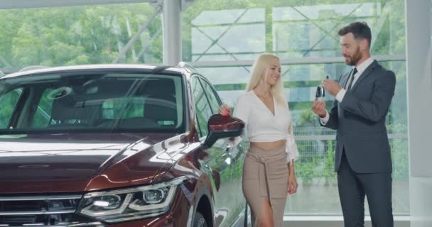 Продавец автомобилей в костюме дает ключи от нового авто счастливой женщине — стоковое видео