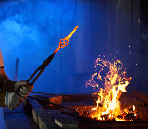 Close up of blacksmith holding forceps with metal over fire