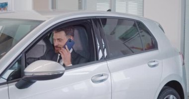 Adam yeni arabasında oturuyor ve kuaförde cep telefonuyla konuşuyor.