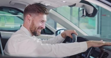 Gülümseyen adam yeni arabasında oturuyor ve parmağını kaldırıyor. 