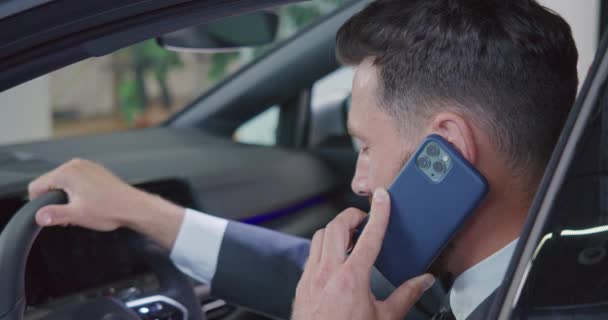 Бизнесмен разговаривает по мобильному телефону при выборе автомобиля в салоне — стоковое видео