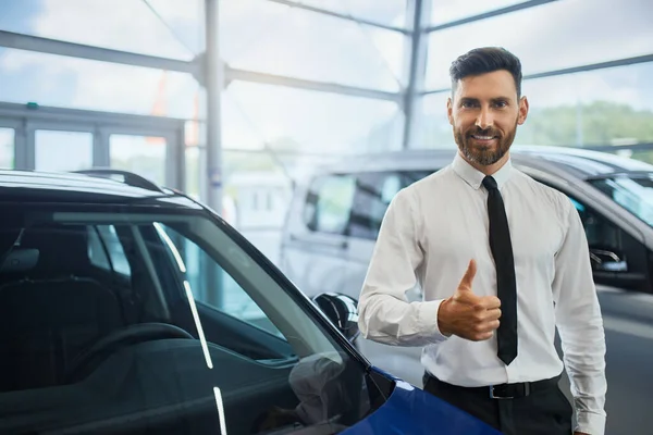 Hombre guapo mostrando el pulgar hacia arriba mientras compra coche en el salón — Foto de Stock