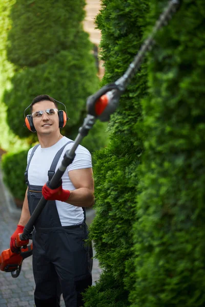 Jardinero usando cortador de gasolina para dar forma a los arbustos al aire libre — Foto de Stock