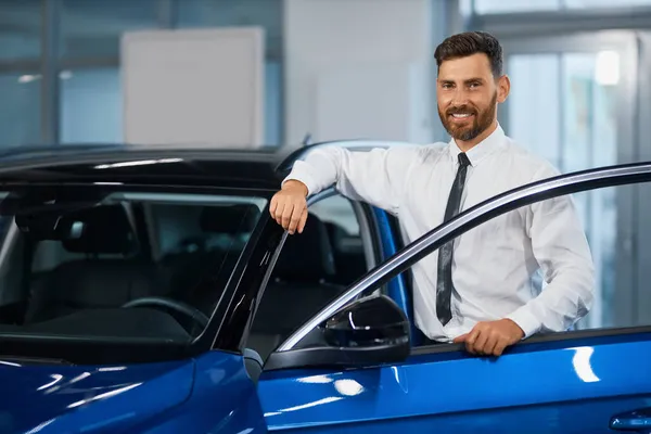 Sorrindo homem no desgaste formal escolhendo carro novo no showroom — Fotografia de Stock