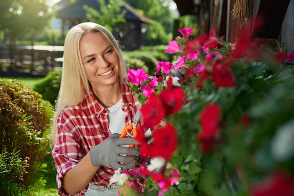 Positieve vrouw tijdens het verzorgen van bloemen in de tuin — Stockfoto