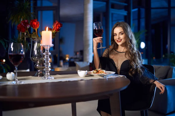 Mulher de vestido preto sentado à mesa com copo de vinho — Fotografia de Stock