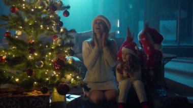 Mutlu anne Noel ağacının yanında küçük kızları kucaklıyor.