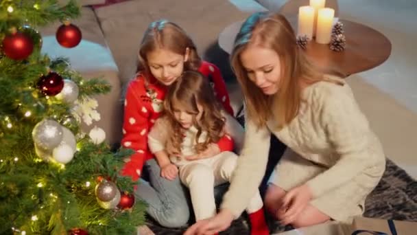 Женщина с дочерьми кладет подарки под елку — стоковое видео