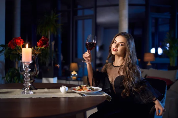 Wunderschöne Frau im schwarzen Kleid mit einem Glas Rotwein — Stockfoto