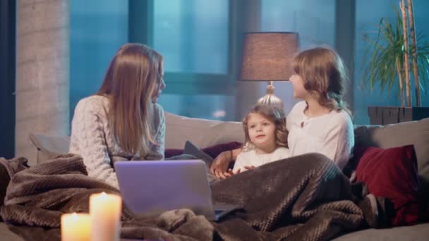 Женщина и две девушки используют ноутбук во время отдыха на диване — стоковое видео